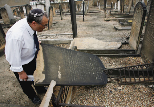 A caretaker inspects the damage in a Jewish cemetery in London, June 2005. (Photo by Graeme Robertson/Getty Images.)