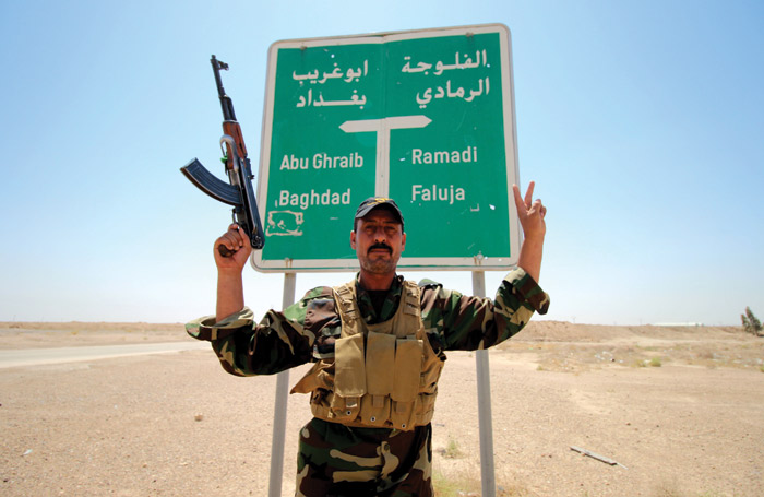 A soldier in the allied Iraqi forces poses in front of a road sign during clashes with Islamic  State group fighters on the outskirts of Fallujah, Anbar province, August 2015. (Photo by  Haidar Mohammed Ali/AFP/Getty Images.) 