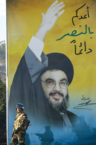 A peacekeeper of the United Nations Interim Force in Lebanon (UNIFIL) stands by a billboard with Hezbollah chief Hassan Nasrallah.