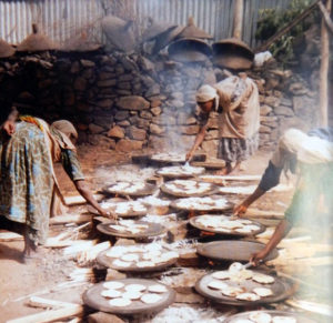 Image shows women preparing matza over open-hair cooking fires. 