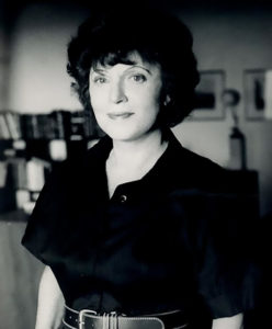 Black and white photo shows Muriel Spark smiling at the camera.