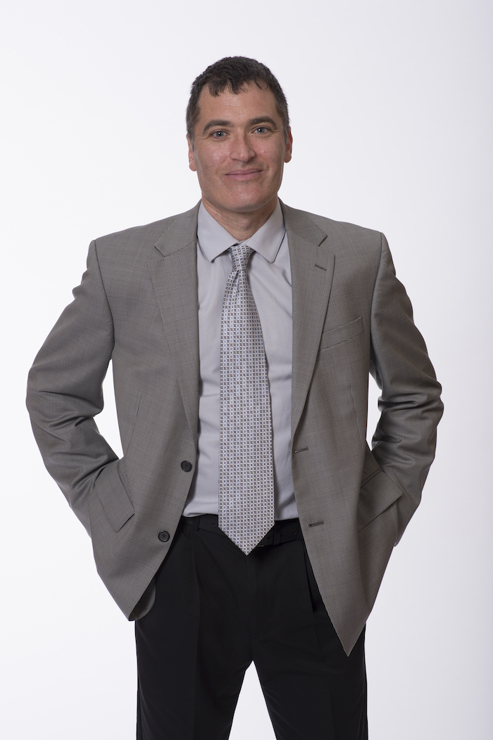 Picture of a man standing in a suit, smiling, plain white background.