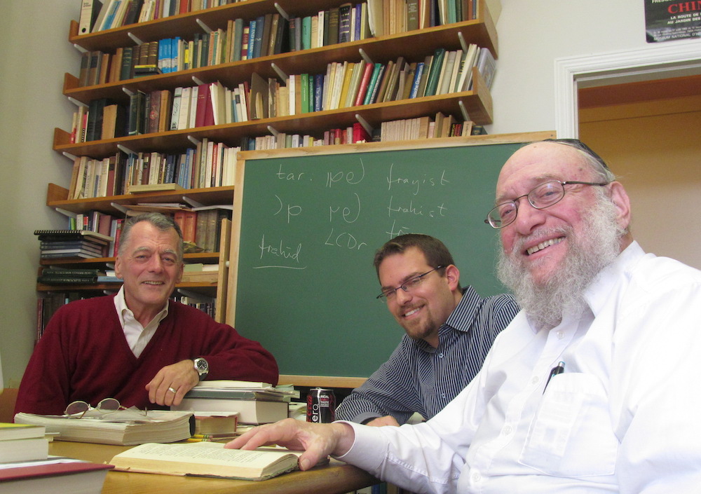 Three men at a classroom table, smiling for the camera.