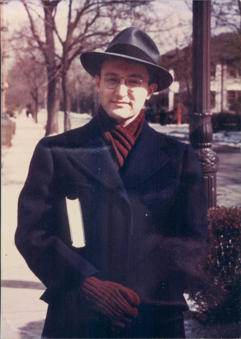Mid-20th-century photograph of a young man outside holding a book.