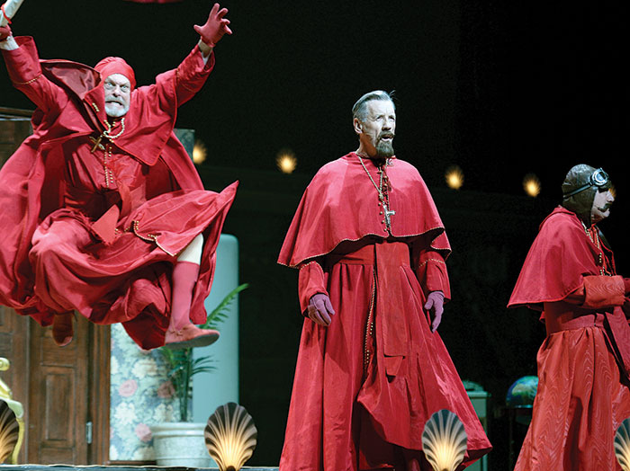 Still photo from Monty Python Live (Mostly), London, 2014. Three actors on stage in red robes.